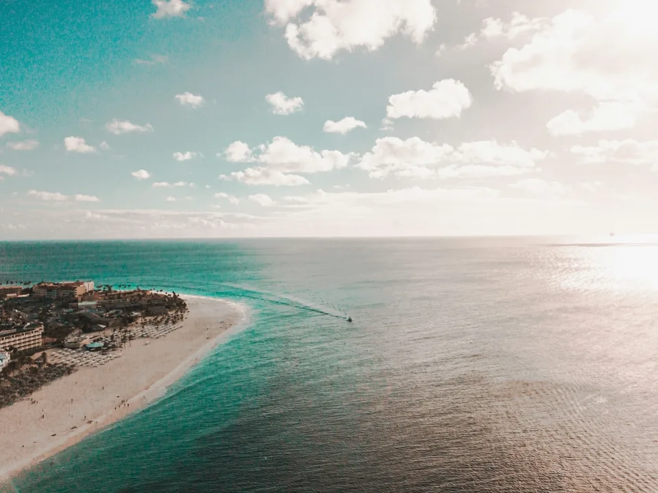 Aerial drone pass along the Aruba shoreline where turquoise shallows meet open sea.
