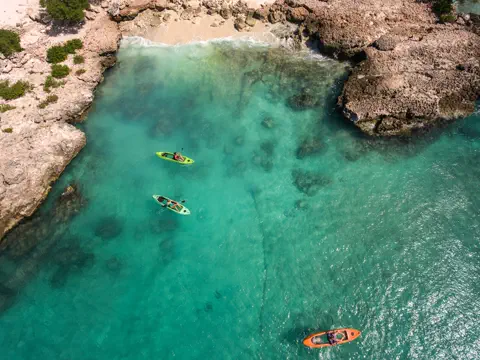 Three kayaks floating in clear turquoise water along Aruba's rocky coast.