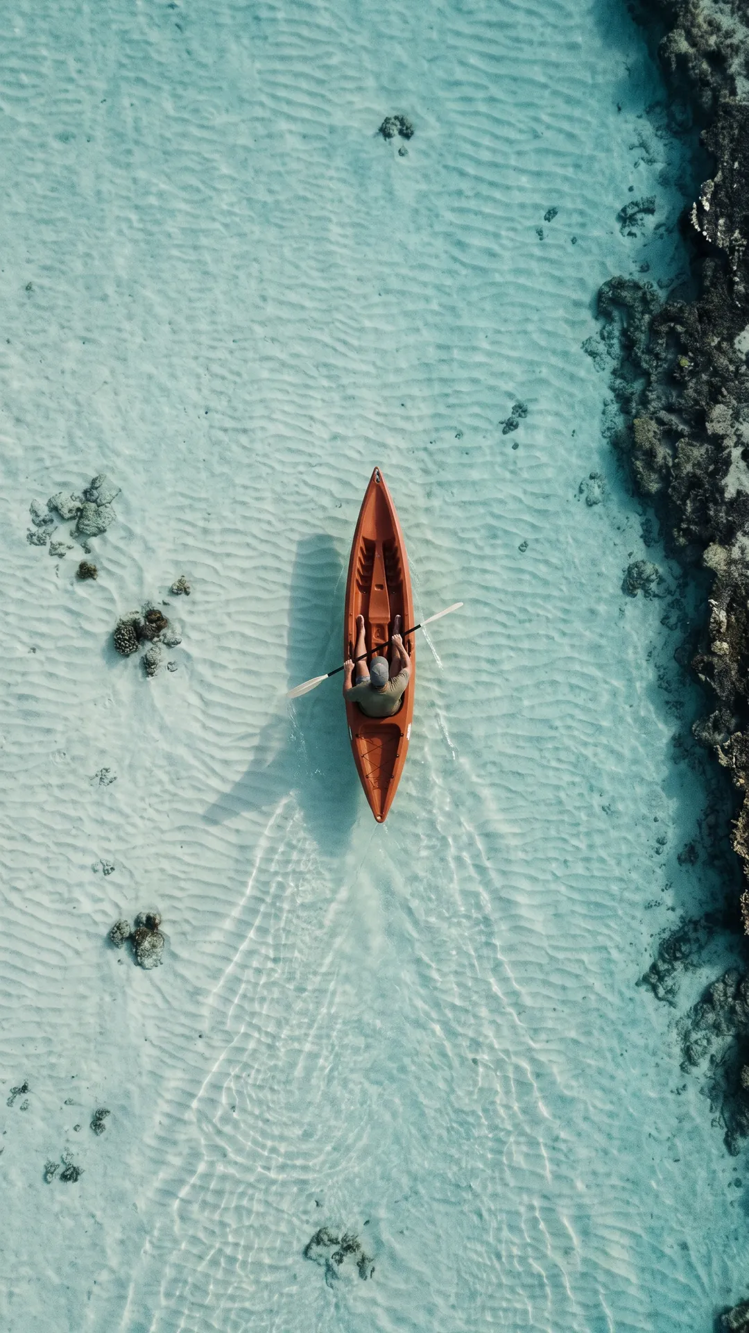Overhead view of an orange kayak crossing clear turquoise shallows.